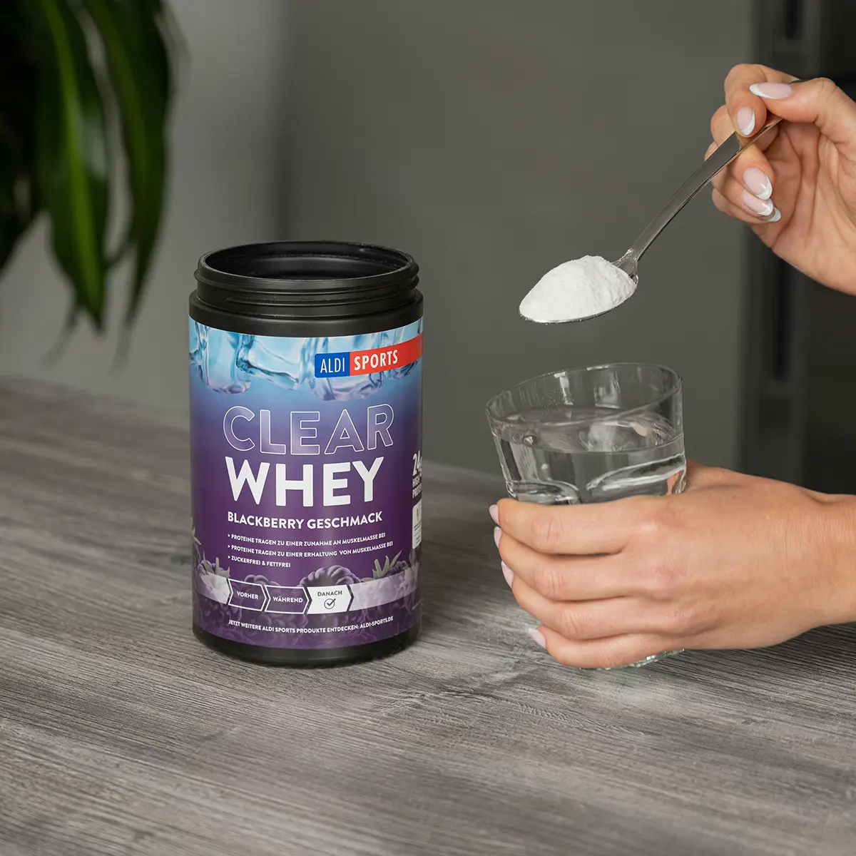 ASP_ClearWhey_Blackberry_04 Clear Whey Pulver Blackberry – Proteinpulver wird aus der Dose in ein Glas gefüllt | Aldi Sports