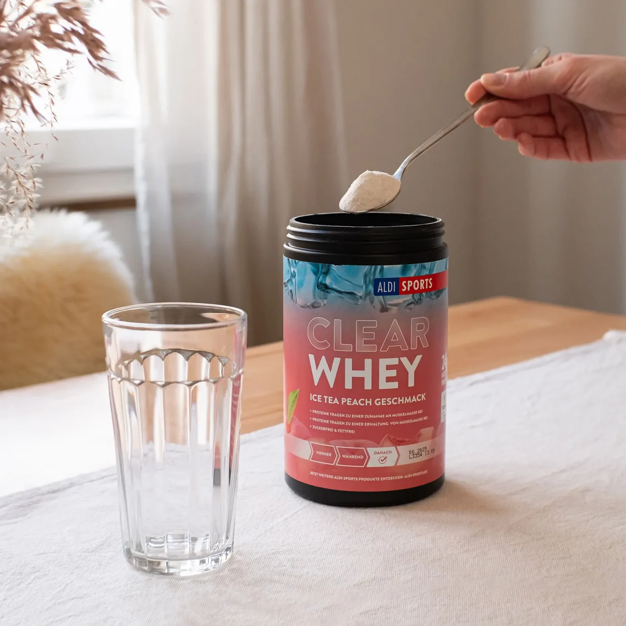 ASP_ClearWhey_IceTeaPeach_01 Clear Whey Pulver Ice Tea Peach – Proteinpulver wird aus der Dose in ein Glas gefüllt | Aldi Sports