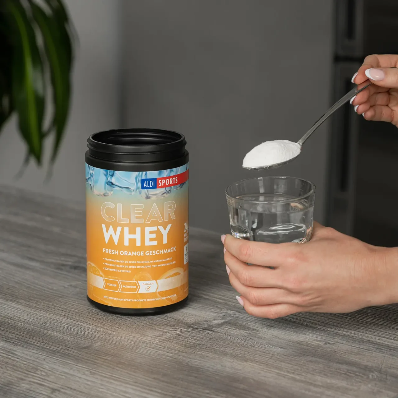 ClearWheyFreshOrange_05.1 Clear Whey Pulver Fresh Orange – Proteinpulver wird aus der Dose in ein Glas gefüllt | Aldi Sports