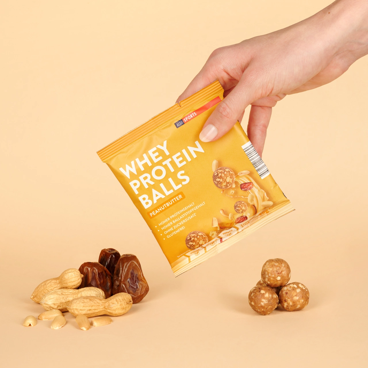 Energy Balls Peanut Butter_04 Whey Protein Balls Peanutbutter – Hand hält die Verpackung, Bälle und Zutaten daneben | Aldi Sports