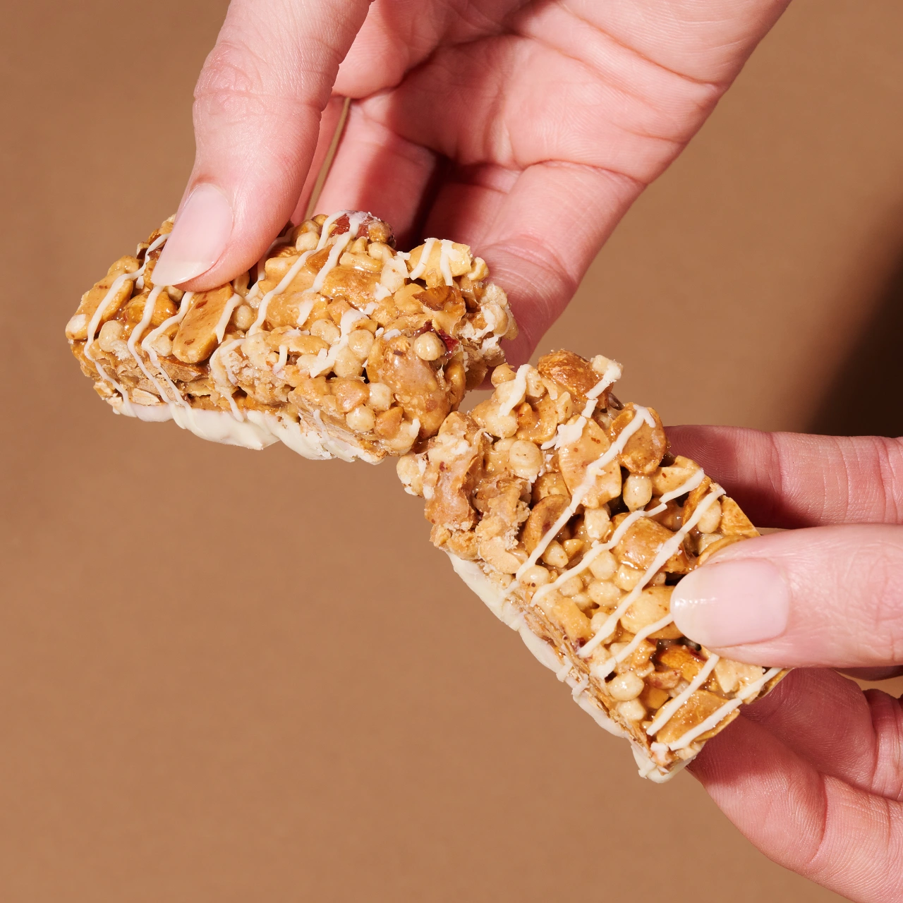 Erdnuss Protein Riegel White Chocolate_04 Erdnuss Protein Riegel White Chocolate Salted Peanut– Hände die einen zerbrochenen Riegel halten | Aldi Sports