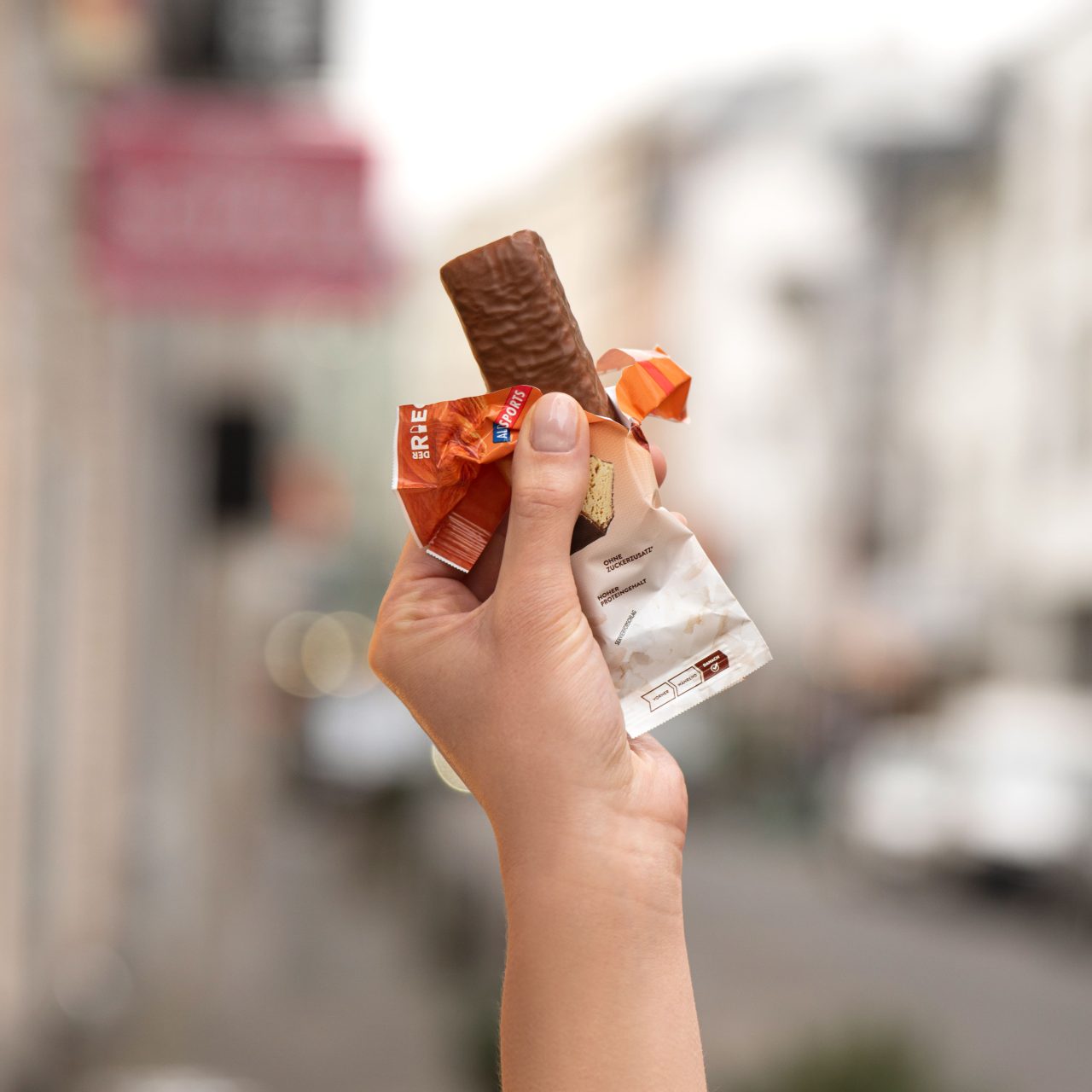 ProteinRiegelKokosMandel_05 Lower Carb Protein Riegel Kokos Mandel – Eine Hand hält den geöffneten Riegel | Aldi Sports